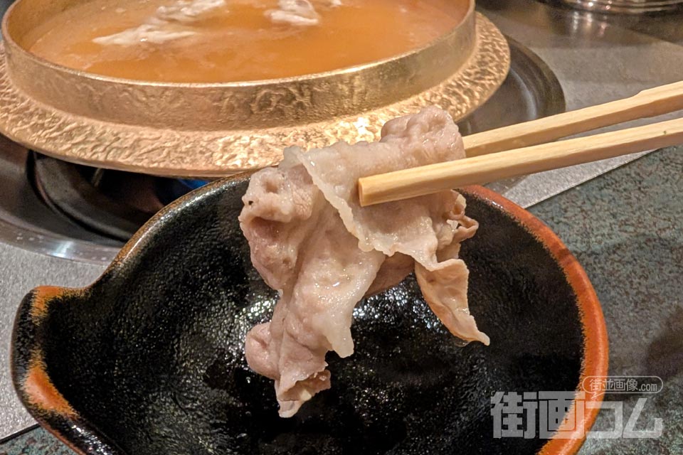取り皿に置いた黒豚バラ肉を箸リフト(背景に鍋)