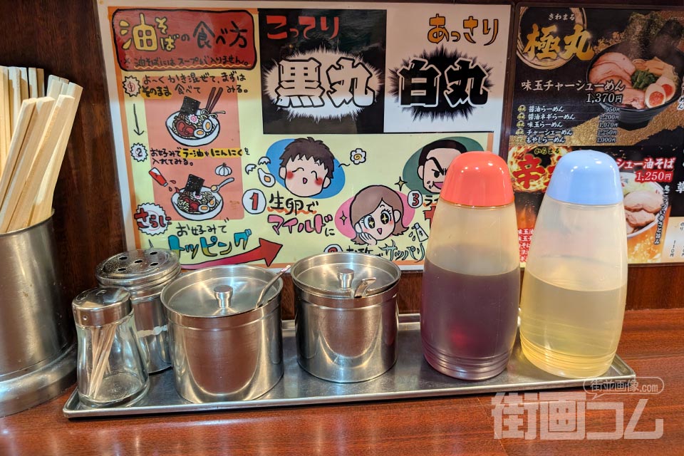 卓上に並ぶ胡椒・おろしにんにく・ラー油・酢と油そばの食べ方の掲示